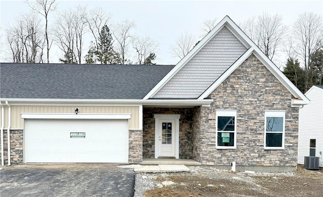 craftsman inspired home featuring central air condition unit, a shingled roof, an attached garage, stone siding, and driveway