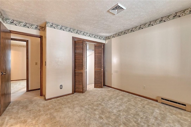 unfurnished bedroom featuring baseboard heating, light carpet, a closet, and a textured ceiling