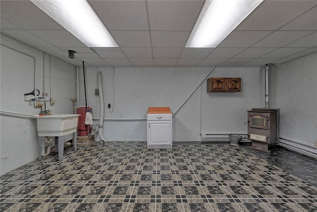 basement featuring baseboard heating, a wood stove, and a drop ceiling