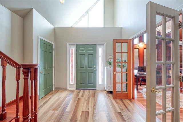 entrance foyer with french doors, a towering ceiling, and light hardwood / wood-style flooring