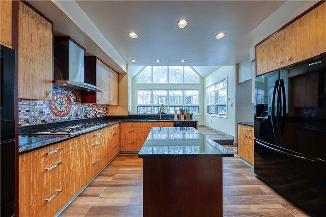 kitchen with a center island, wall chimney exhaust hood, sink, light hardwood / wood-style floors, and black fridge with ice dispenser