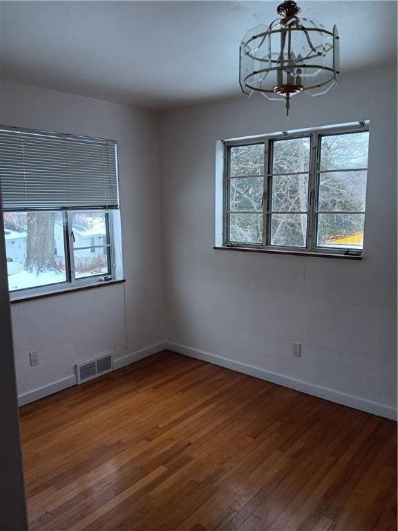 empty room with hardwood / wood-style floors and a notable chandelier