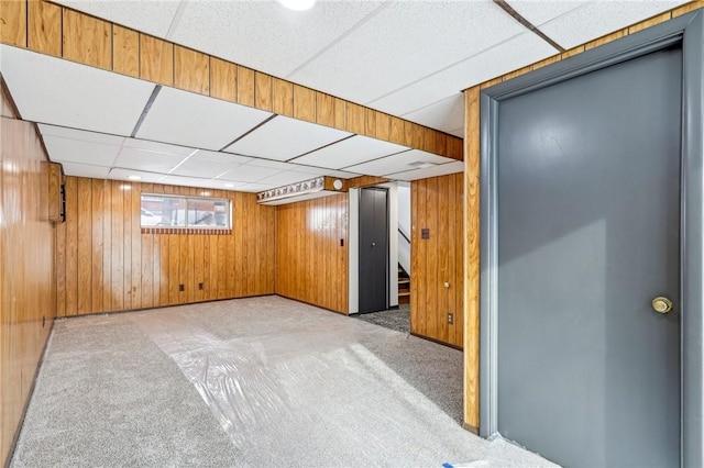 basement with light carpet, a paneled ceiling, and wood walls