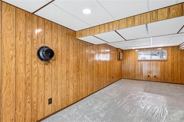 basement with light carpet, a paneled ceiling, and wooden walls