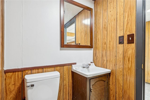 bathroom with wooden walls, vanity, and toilet