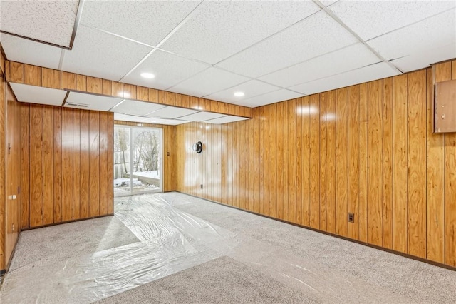 basement featuring a paneled ceiling, wooden walls, and light colored carpet