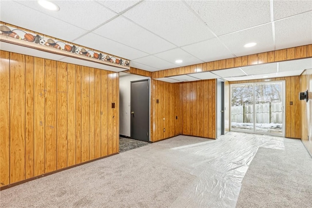 interior space with a paneled ceiling, light colored carpet, and wood walls