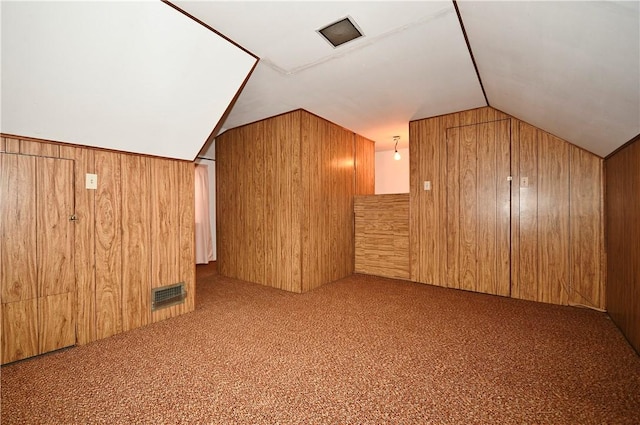 additional living space with vaulted ceiling, light colored carpet, and wooden walls