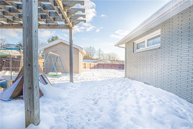 yard layered in snow with a pergola, a playground, and a storage unit