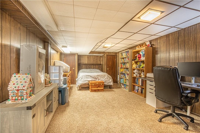 carpeted bedroom featuring a paneled ceiling and wood walls