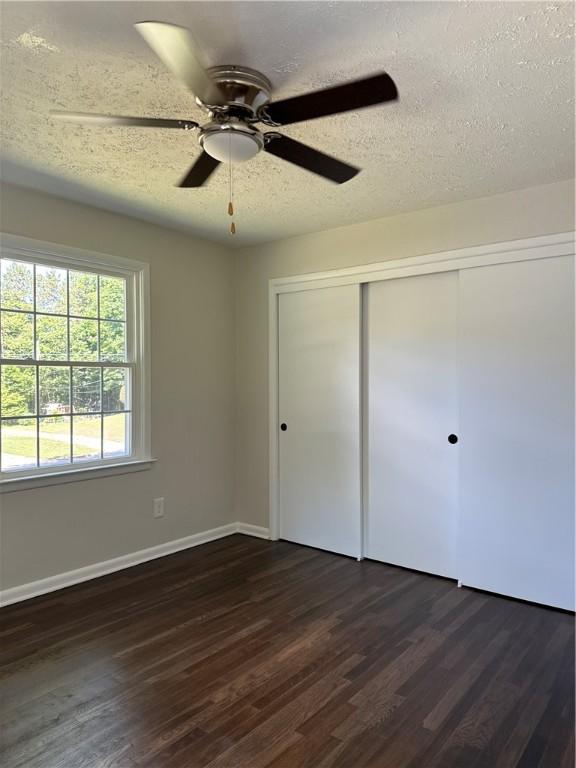 unfurnished bedroom with ceiling fan, dark hardwood / wood-style floors, a textured ceiling, and a closet