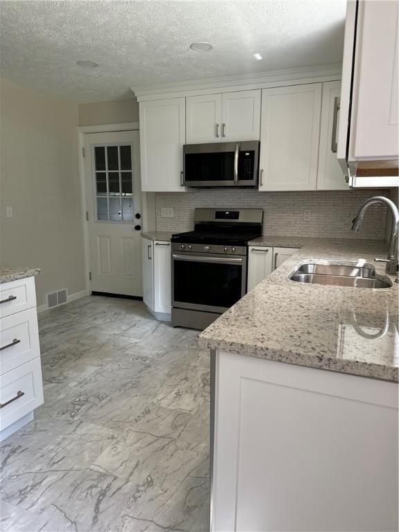 kitchen with backsplash, light stone counters, stainless steel appliances, sink, and white cabinetry