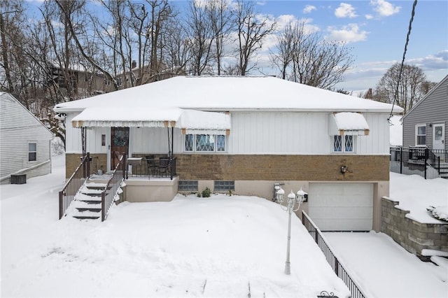 snow covered rear of property with a garage and central AC unit