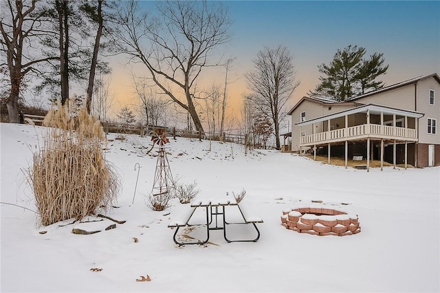 yard layered in snow with a deck, an outdoor fire pit, and a sunroom