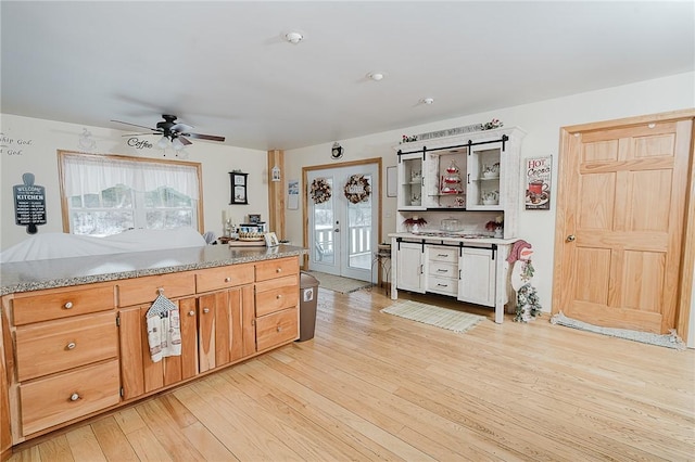 kitchen featuring ceiling fan, light stone counters, light wood-type flooring, and french doors