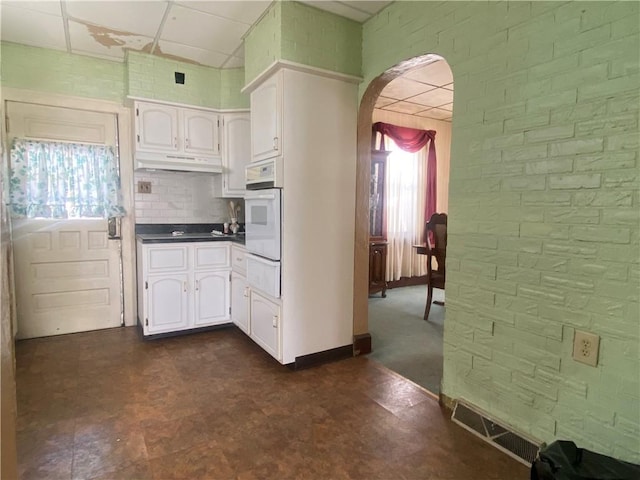 kitchen with a paneled ceiling, white cabinetry, oven, and brick wall