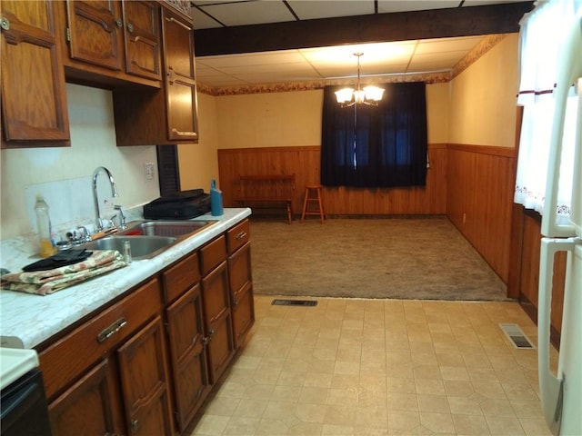 kitchen featuring wood walls, light carpet, sink, hanging light fixtures, and a chandelier