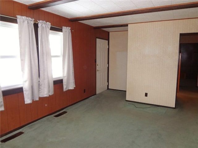 carpeted empty room with wood walls and beam ceiling