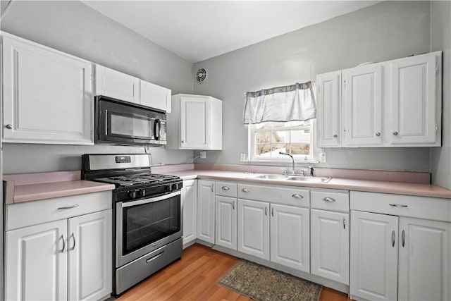 kitchen featuring a sink, stainless steel range with gas cooktop, black microwave, and light countertops