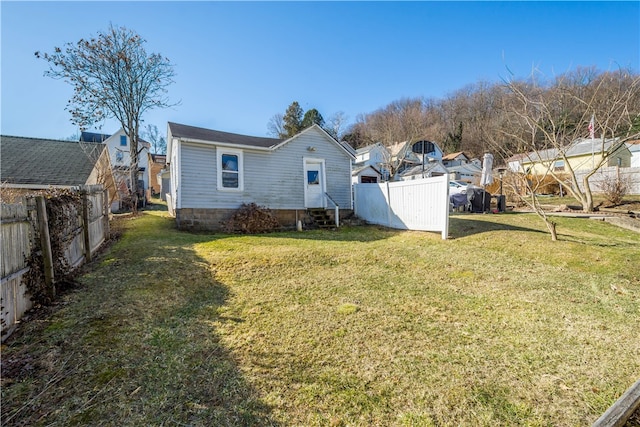 rear view of house featuring entry steps, a yard, and fence