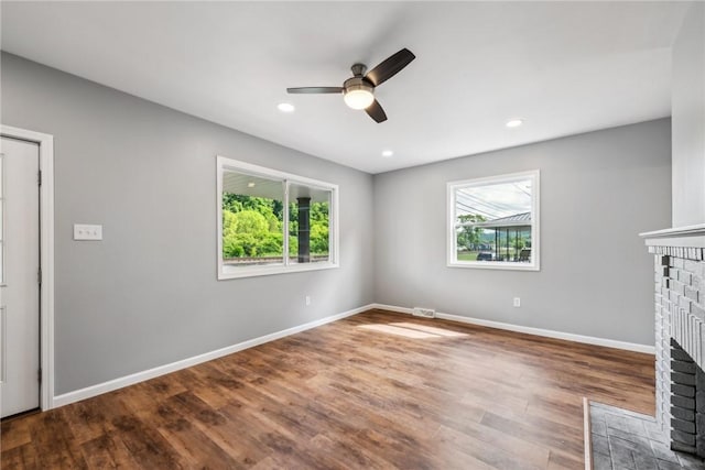 unfurnished living room featuring ceiling fan, hardwood / wood-style floors, a healthy amount of sunlight, and a brick fireplace