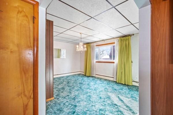 empty room featuring a paneled ceiling, carpet floors, a chandelier, and a baseboard heating unit