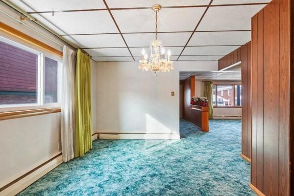 carpeted empty room with a baseboard heating unit and a chandelier