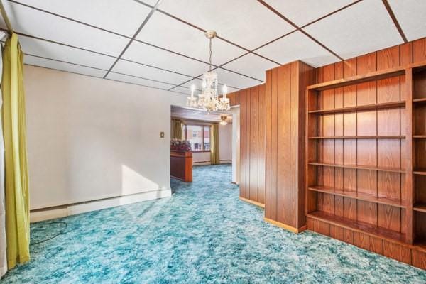 unfurnished room featuring a chandelier, carpet floors, a paneled ceiling, and wood walls