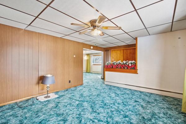 carpeted empty room featuring ceiling fan and a baseboard heating unit