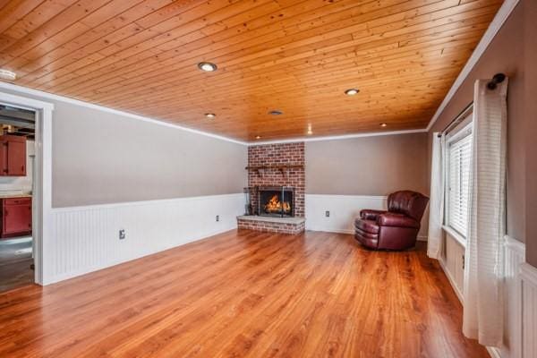 unfurnished living room featuring light hardwood / wood-style flooring, wood ceiling, ornamental molding, and a brick fireplace