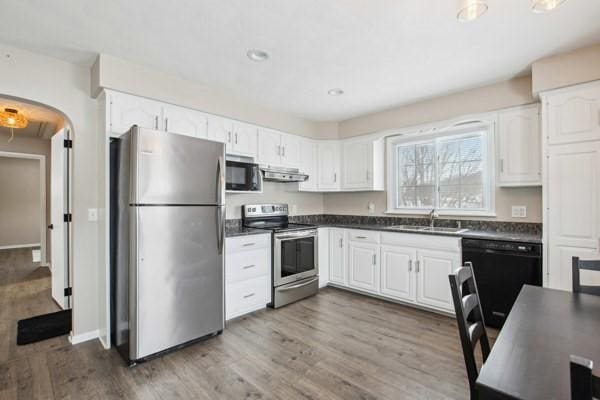 kitchen with white cabinetry, sink, extractor fan, black appliances, and hardwood / wood-style flooring