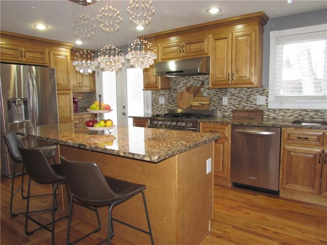 kitchen featuring pendant lighting, a center island, wood-type flooring, stainless steel appliances, and a chandelier