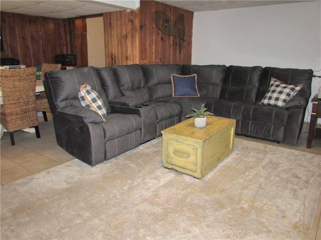 living room with a paneled ceiling, light tile patterned flooring, and wood walls