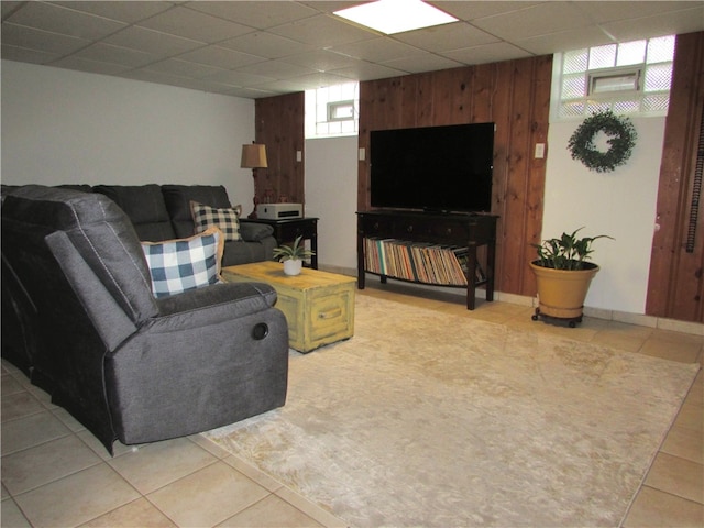 living room featuring light tile patterned floors, a paneled ceiling, and wooden walls