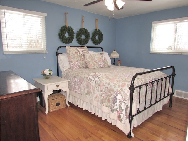 bedroom with ceiling fan, multiple windows, and dark hardwood / wood-style flooring