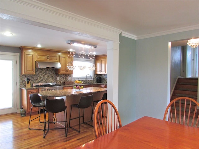 kitchen featuring dark stone countertops, light hardwood / wood-style floors, a kitchen breakfast bar, sink, and ornamental molding