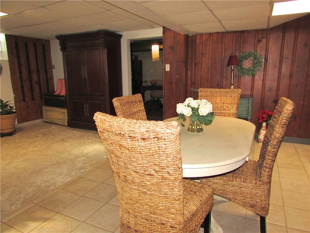 dining area with light tile patterned flooring, a drop ceiling, and wooden walls