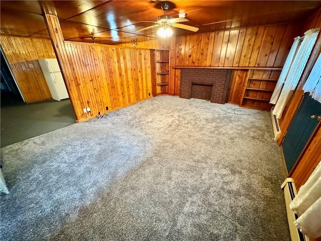 living room featuring ceiling fan, dark carpet, a fireplace, and wooden walls