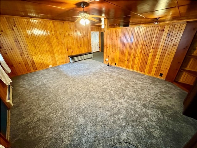 basement with radiator, wood walls, ceiling fan, and dark carpet