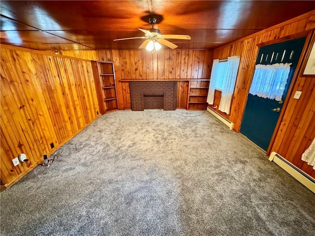 unfurnished living room with baseboard heating, wood walls, carpet flooring, and a brick fireplace