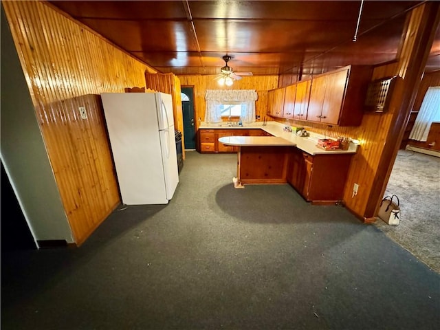 kitchen featuring kitchen peninsula, ceiling fan, wooden walls, white refrigerator, and carpet floors