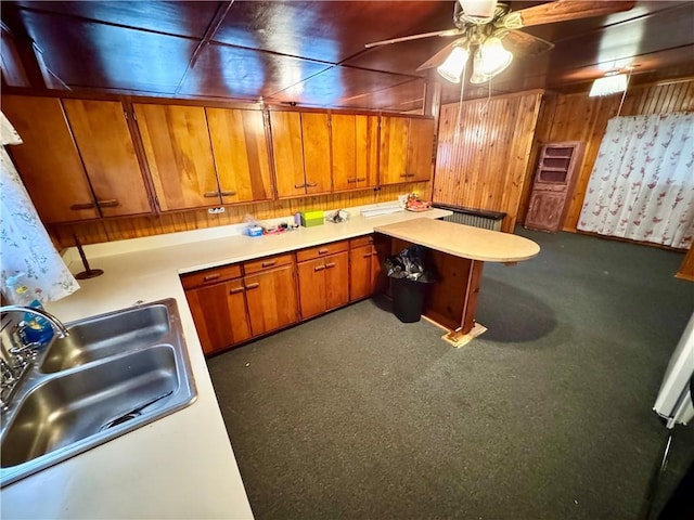 kitchen with dark colored carpet, sink, ceiling fan, and wood walls