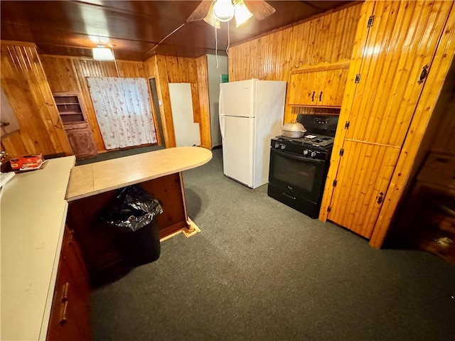 kitchen featuring black gas range oven, white refrigerator, ceiling fan, and wooden walls