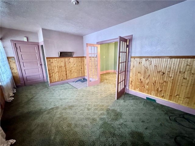 interior space featuring carpet, french doors, a textured ceiling, and wooden walls