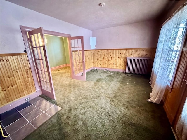 carpeted empty room with radiator heating unit, wooden walls, and french doors