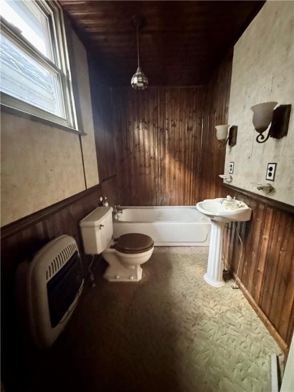 bathroom with a bathing tub, wood walls, toilet, and heating unit