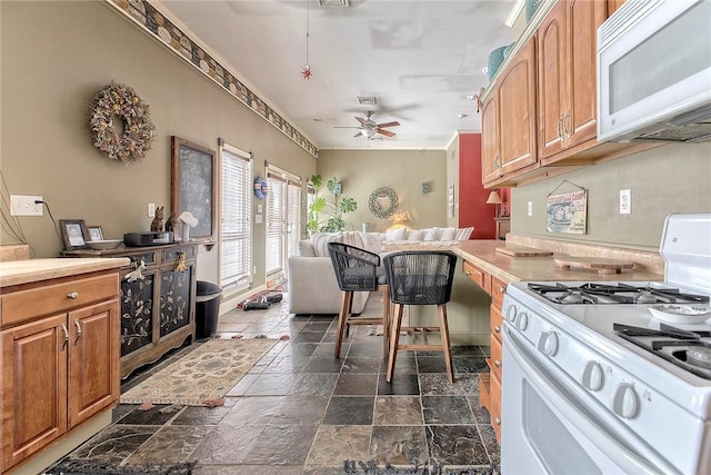 kitchen featuring a kitchen bar, white appliances, ceiling fan, and ornamental molding