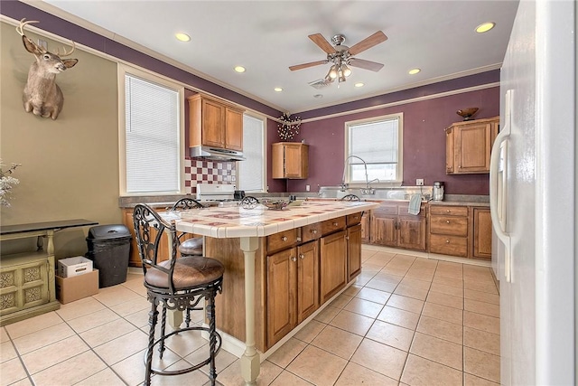 kitchen with ceiling fan, white refrigerator, a center island, tile counters, and light tile patterned flooring