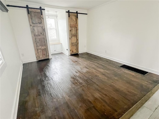 unfurnished bedroom with a barn door, crown molding, and dark wood-type flooring