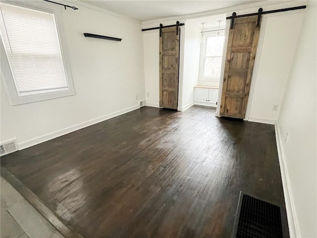 unfurnished room featuring a barn door, crown molding, and dark wood-type flooring